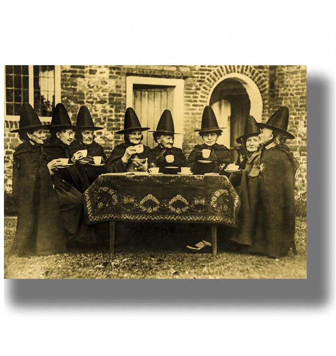 Vintage photograph of women dressed as witches sitting around a table and drinking tea outdoors.