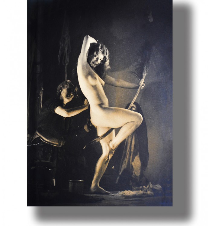 Vintage photograph of a nude woman posing with a broomstick in a witch sabbath scene.