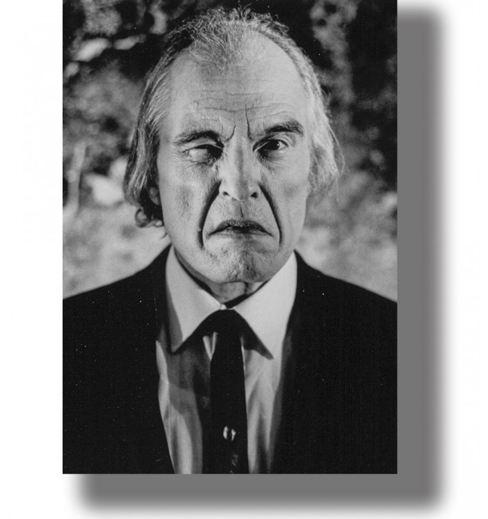 Black and white close-up portrait of an older man in a dark suit with an intense and sinister expression.