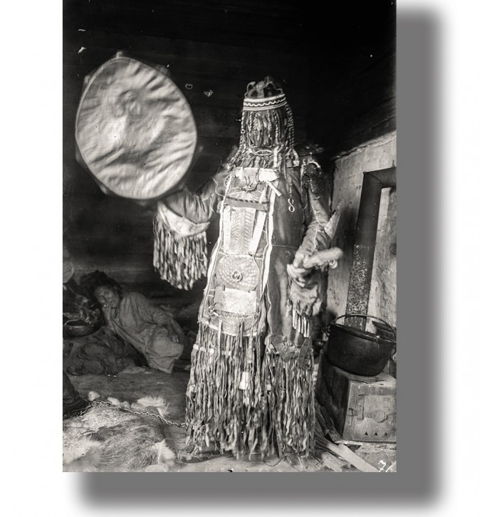 Vintage black and white photo of a Siberian shaman holding a drum inside a dwelling.