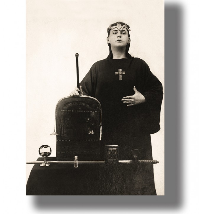 Vintage photo of Aleister Crowley in ritual robes standing by an altar with occult objects.