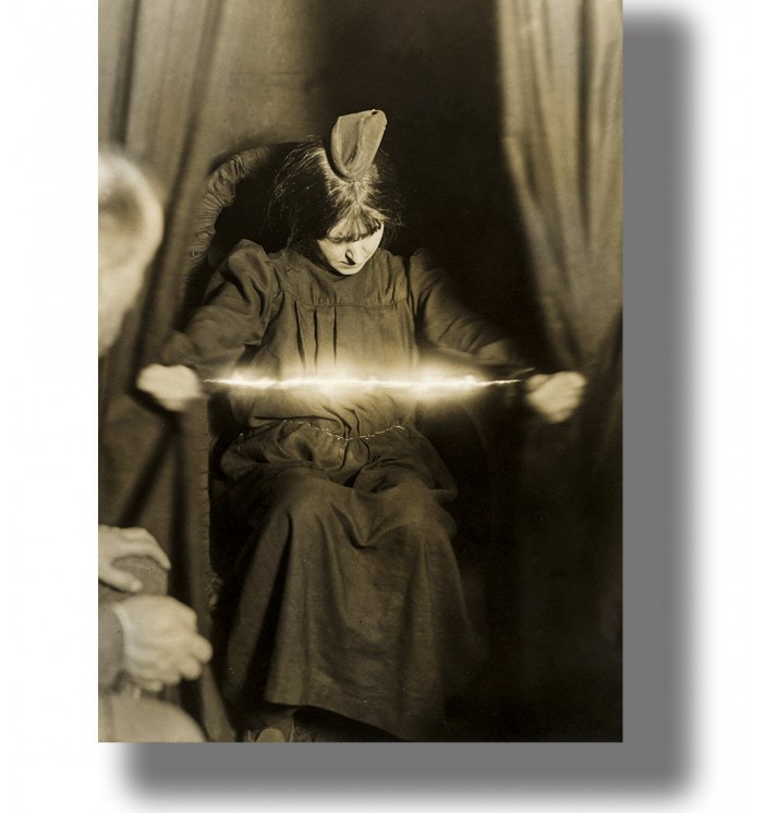 Vintage sepia séance photograph of Eva Carrière seated in a chair, holding a glowing band-like form between her hands.