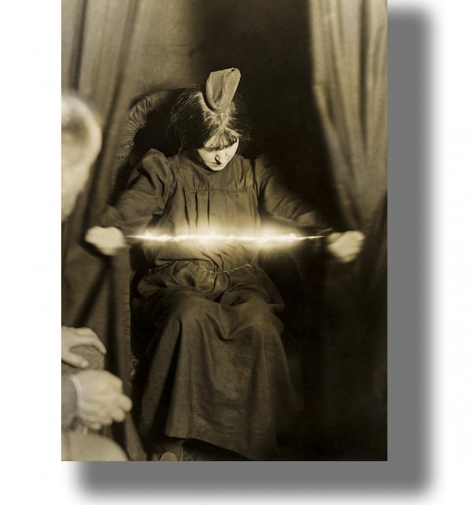 Vintage sepia séance photograph of Eva Carrière seated in a chair, holding a glowing band-like form between her hands.