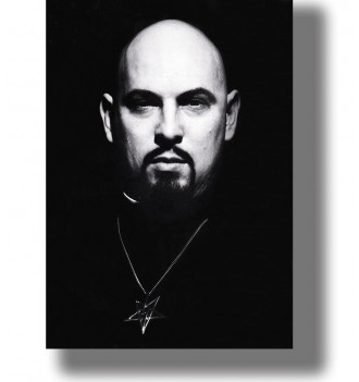 Black and white portrait of Anton LaVey with a shaved head, dark goatee and pentagram pendant against a black background.
