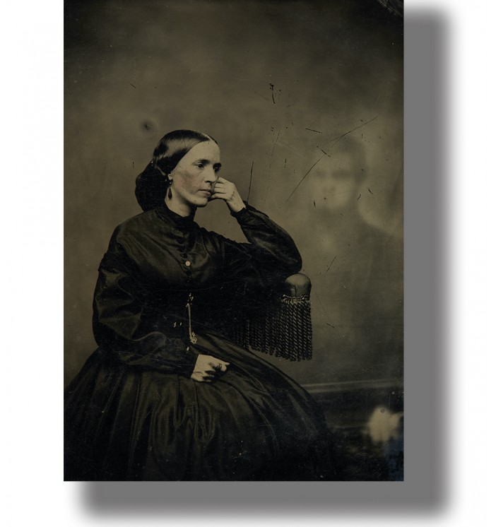 Old Victorian-style photo of a woman seated in black dress with a faint ghostly figure behind her.