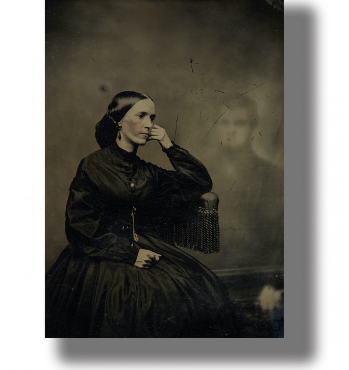 Old Victorian-style photo of a woman seated in black dress with a faint ghostly figure behind her.