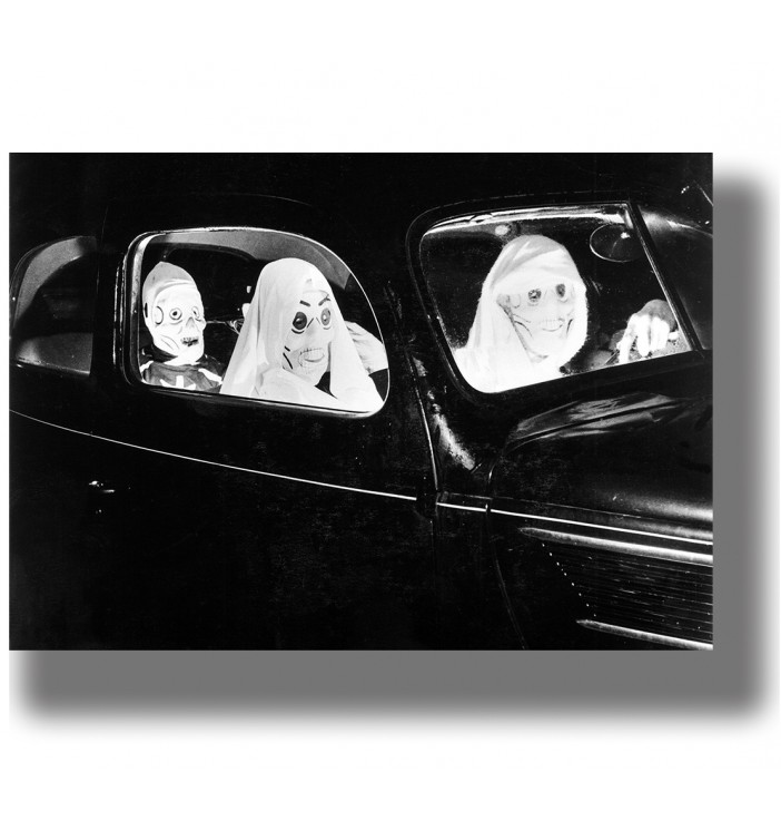 Black and white vintage photo of people wearing creepy Halloween masks and costumes while sitting inside an old car.