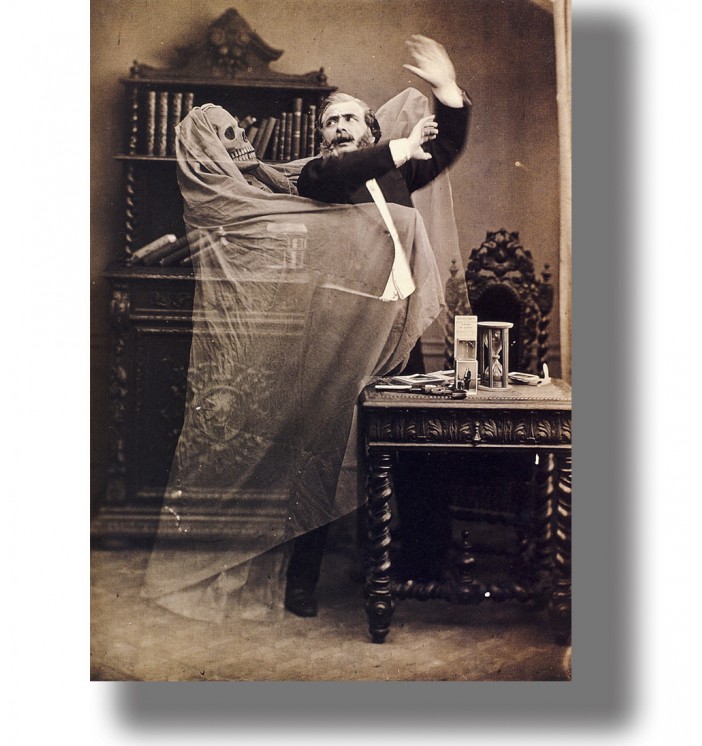 Vintage spirit photo of a man recoiling from a ghostly skeleton figure draped in transparent fabric.