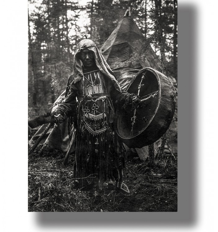 Black and white photograph of a Siberian shaman with a drum standing in a forest camp.