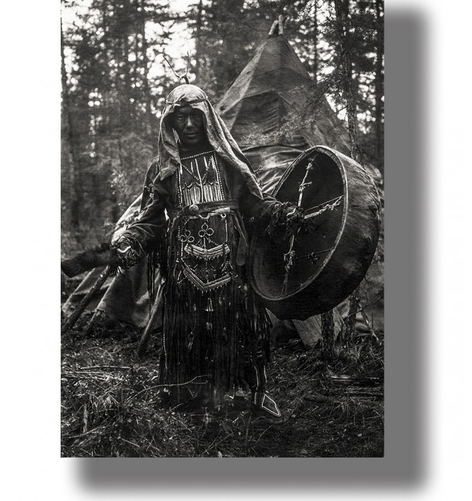 Black and white photograph of a Siberian shaman with a drum standing in a forest camp.