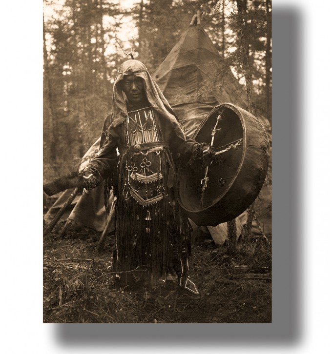 Black and white photograph of a Siberian shaman with a drum standing in a forest camp.